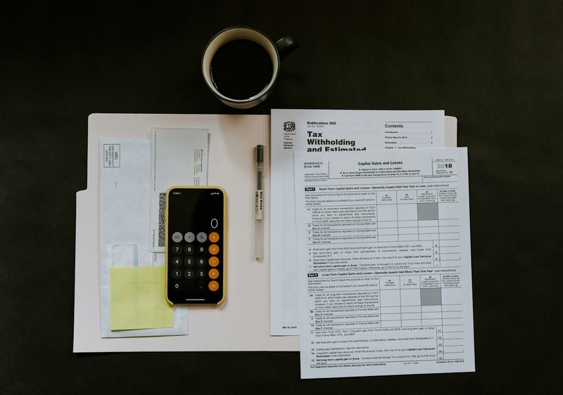 Formulários fiscais, calculadora no celular e café sobre uma mesa escura